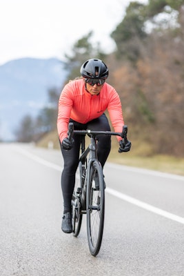 Cyclist wearing a fluro orange jacket riding on a road.