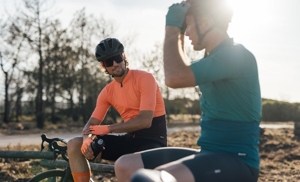 Two cyclists taking a break, one wearing an orange jersey and the other a teal jersey.